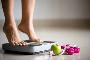 Pessoa se pesando na balança depois de fazer um curso de emagrecimento