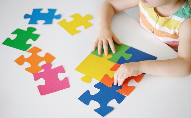 Criança com autismo infantil montando um quebra-cabeça colorido