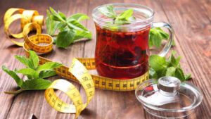 Imagem com um copo de chá para secar barriga e uma fita métrica em volta