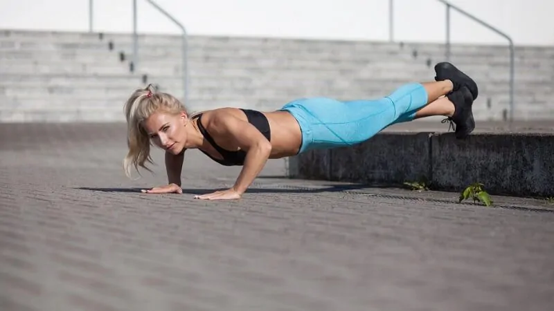 imagem com uma mulher fazendo flexão com os pés levantados para treino de ombros