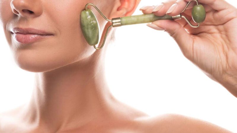 imagem de uma mulher usando o rolo de jade para massagear a face