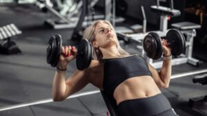 imagem com uma mulher realizando o exercício supino inclinado com halteres