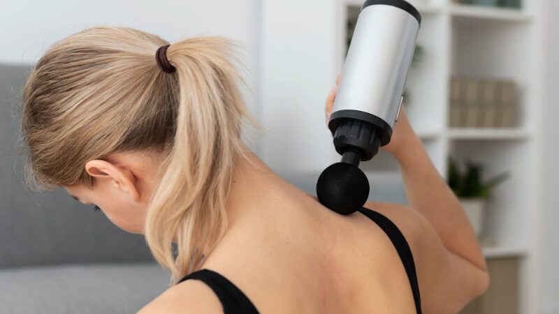Imagem de uma mulher utilizando um massageador elétrico nas costas