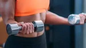 imagem com uma mulher realizando o exercício rosca direta com halteres