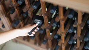 a mão de uma pessoa puxando uma garrafa de vinho de uma adega de madeira