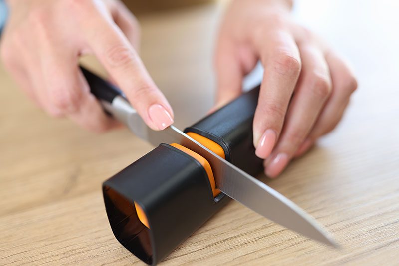 mãos de uma mulher afiando uma faca com um afiador de cozinha