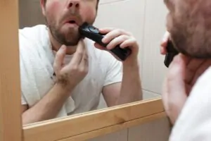 Homem utilizando um aparelho de barbear em frente ao espelho do banheiro