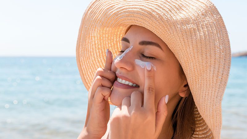 Imagem de uma mulher aplicando protetor solar no rosto